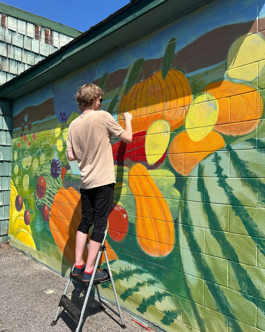 Pintura mural en ejecución sobre un muro exterior, con la mano sujetando un pincel cargado de color